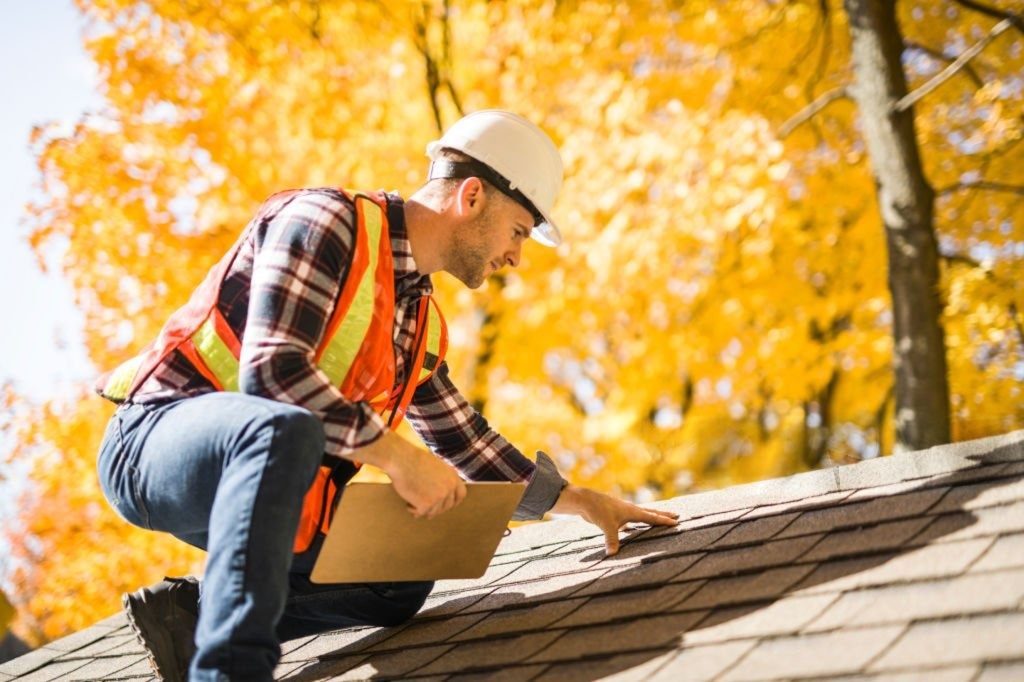 Roofing inspector in a hard hat and safety vest examining shingles on a residential roof