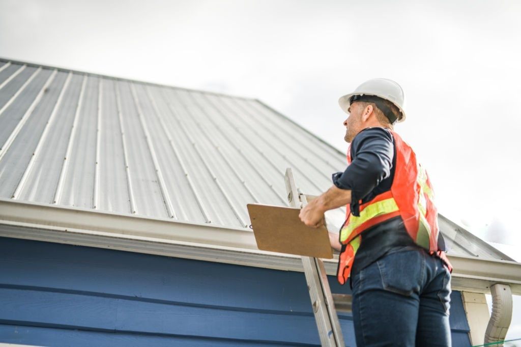 Roofing inspector climbing a ladder to examine a metal roof on a blue house