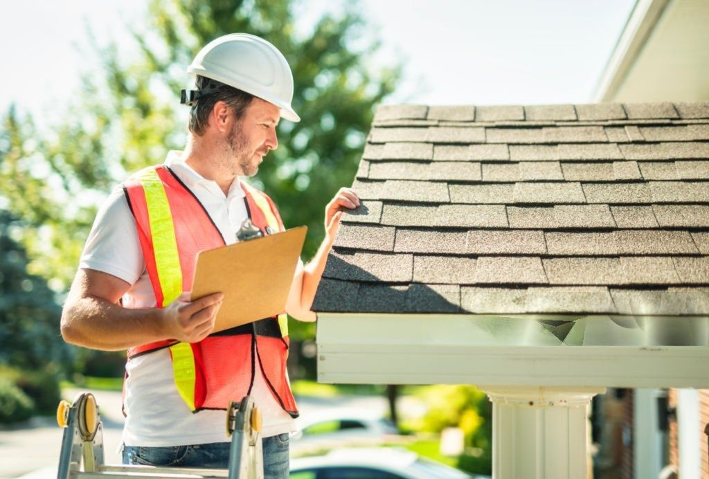 Roofing professional with a clipboard checking shingle condition on a residential roof