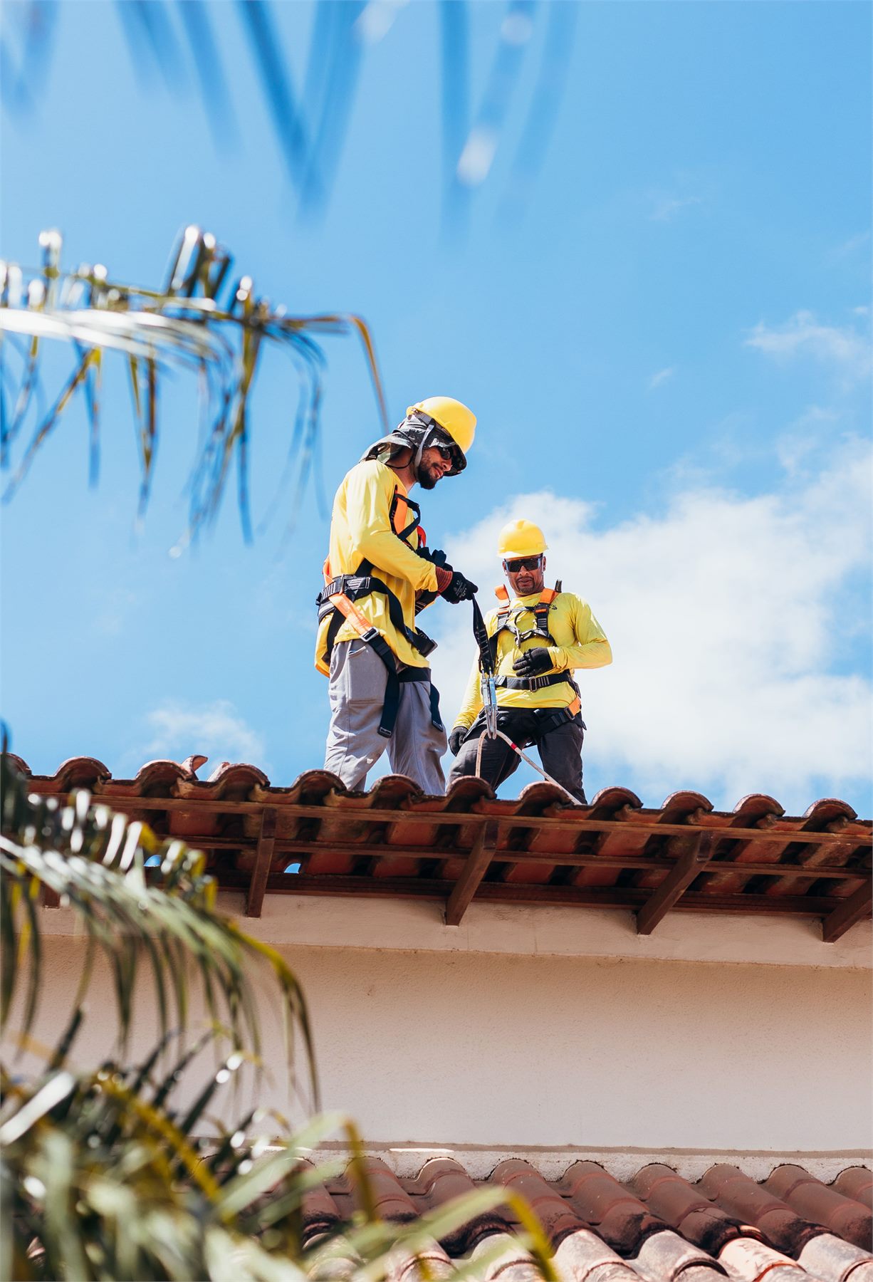 Roofing crew in safety harnesses working along the ridge of a tile roof